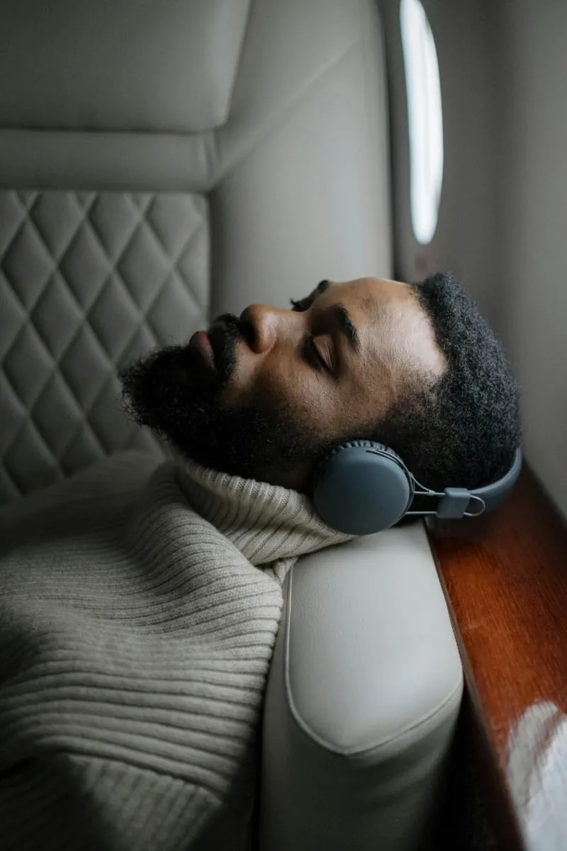 A man reclined in a padded treatment chair, headphones on and eyes closed, resting.